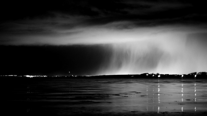 Nighttime rain over a body of water with city lights