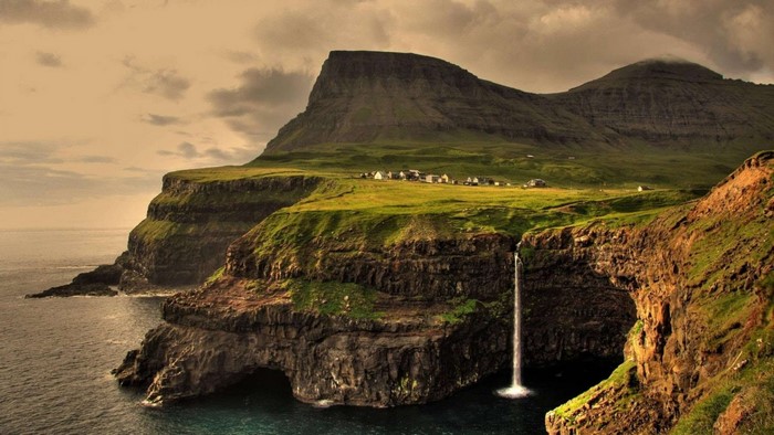 Waterfall cascading from cliffs into the sea near a village