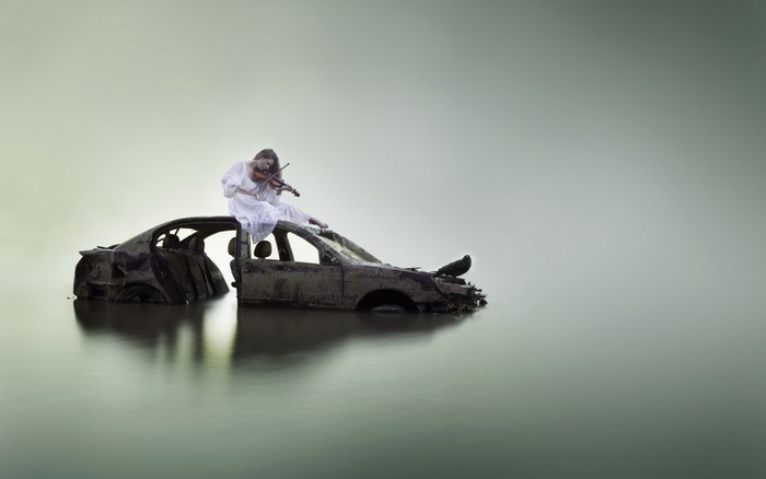 Woman in white dress playing violin on submerged car
