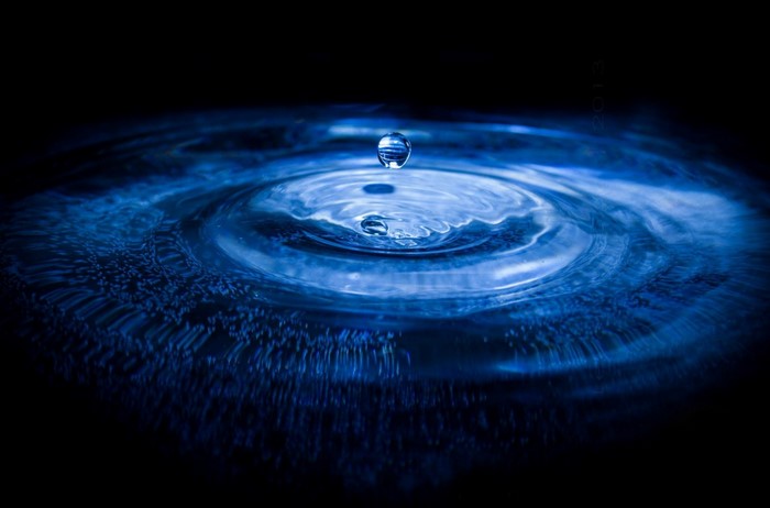 Water drop creating ripples in dark blue water