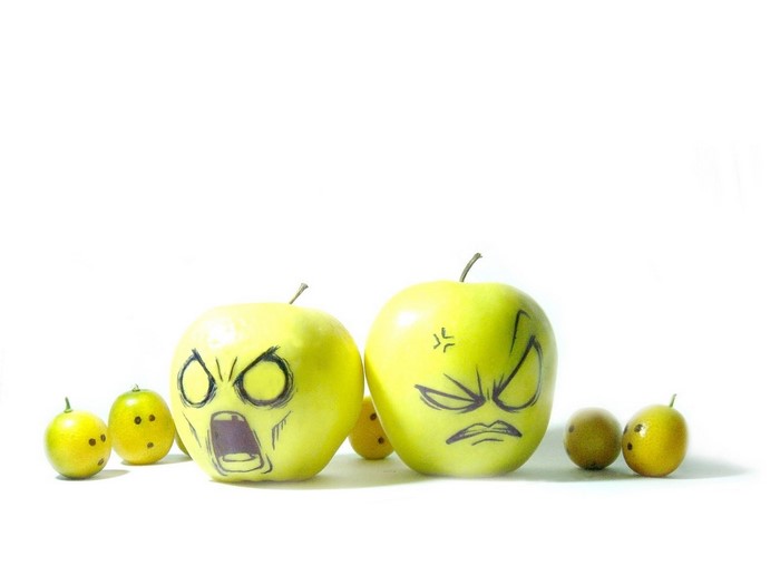 Two apples with faces drawn on them and small fruits