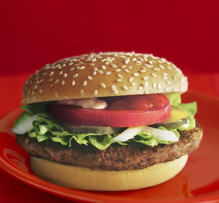 Hamburger with lettuce, tomato, pickles, and onions on a sesame seed bun