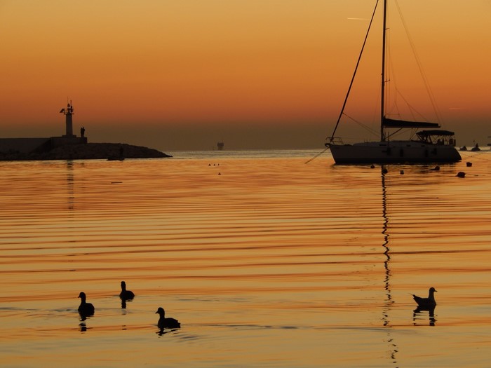 Sailboat and lighthouse at sunset over the sea