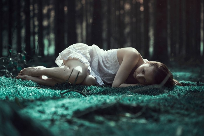 Woman in white dress lying on grass in forest
