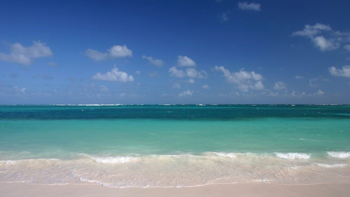Turquoise ocean waves on a sandy beach under a blue sky
