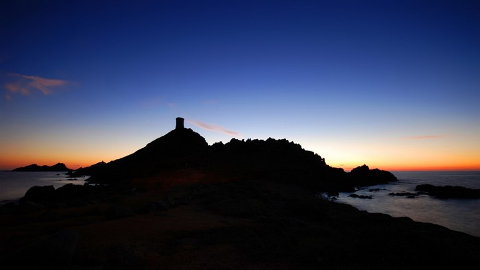 Silhouette of a tower on a rocky island at sunset