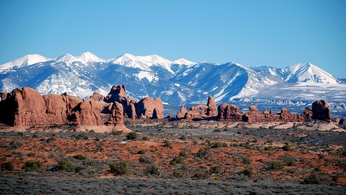 Red rock formations and snow-capped mountains under a clear blue sky