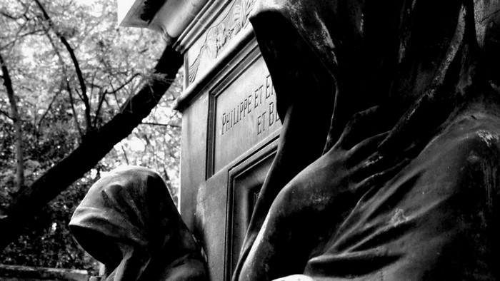 Monochrome statue of cloaked figures in a cemetery