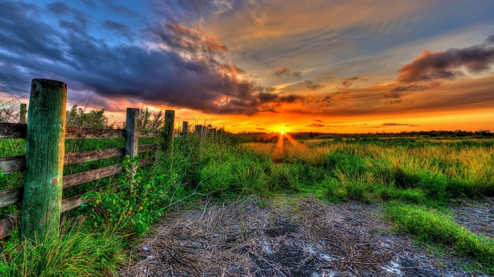 Sunset over a grassy field with a wooden fence