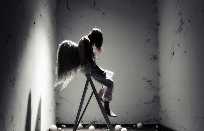 Angel with wings sitting on a ladder in a dark room