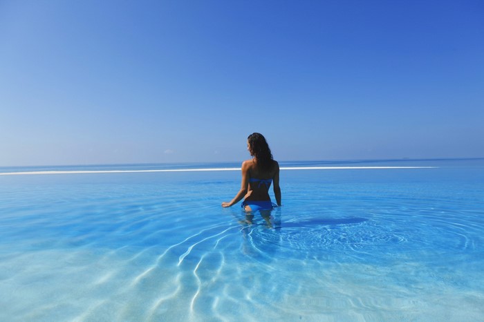 Woman in blue bikini in infinity pool overlooking the ocean