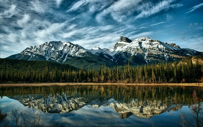 Snow-capped mountains reflected in a calm lake with pine trees