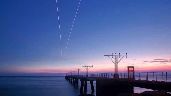 Airplane contrails over ocean pier at dusk