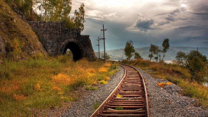 Railroad tracks leading to a stone tunnel in autumn landscape