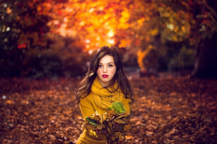 Young woman in yellow scarf holding autumn leaves