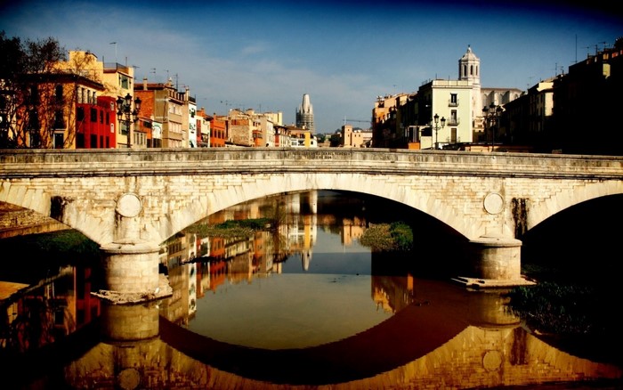 Stone bridge over a river with city buildings and reflections