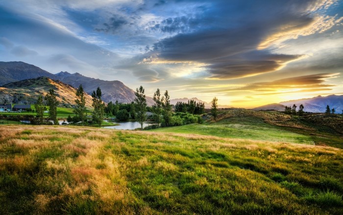 Sunset over a grassy landscape with mountains and a lake