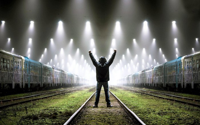 Man with arms raised between two trains at a station