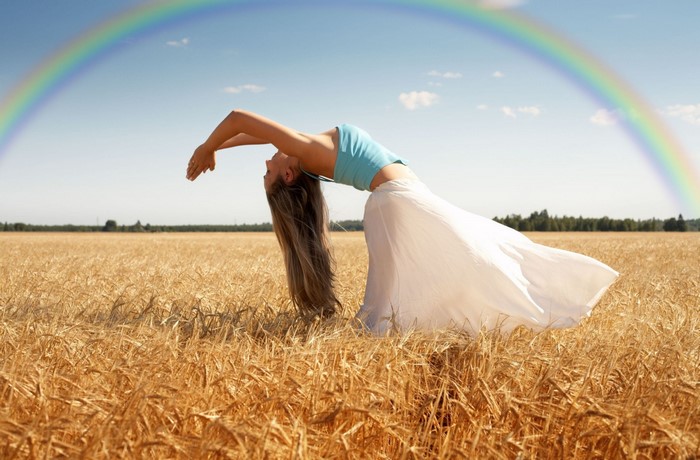 Woman arching back in wheat field with rainbow