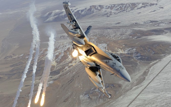 Boeing EA-18G Growler releasing flares over desert landscape
