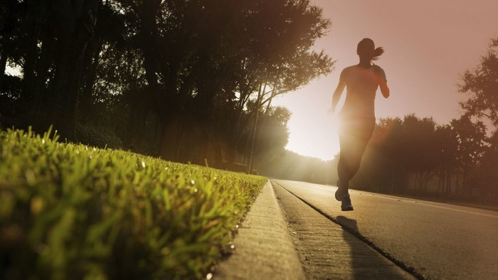 Woman running on road at sunset with sun flare