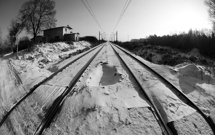 Snowy railway tracks leading to the horizon with a building on the left