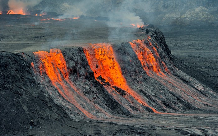 Molten lava flowing down a volcanic slope with a person observing