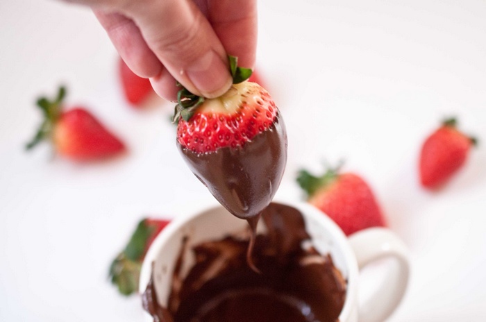 Chocolate-dipped strawberry being held over a mug