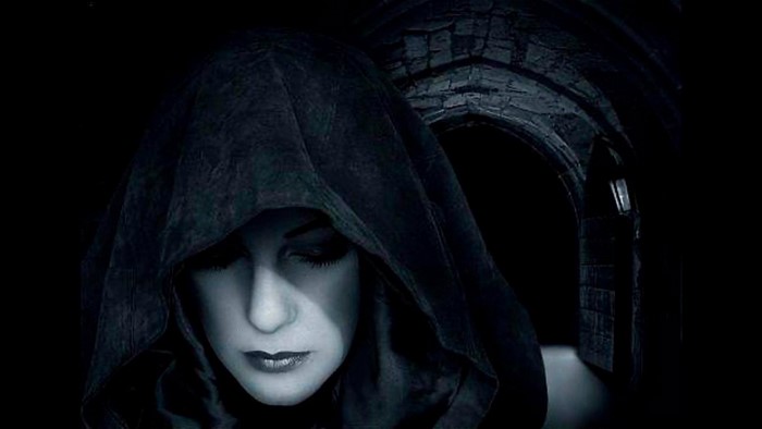 Woman in a black hood in a dark stone archway
