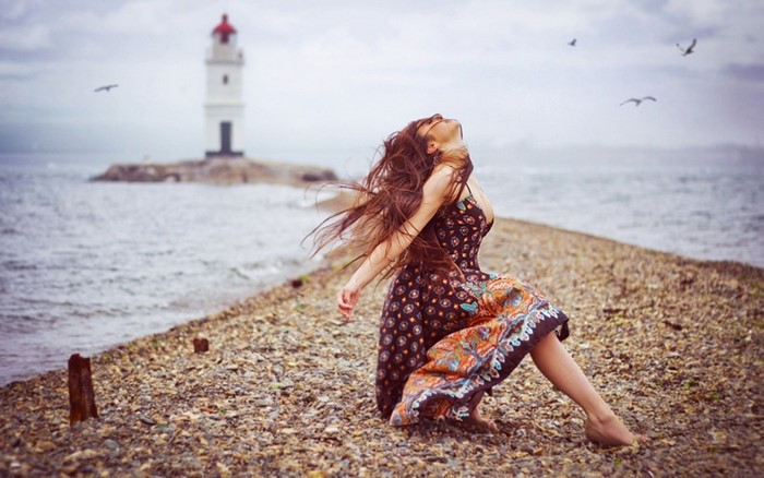 Woman with long hair by the sea with lighthouse