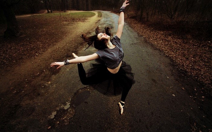 Woman in ballet attire jumping on a forest road
