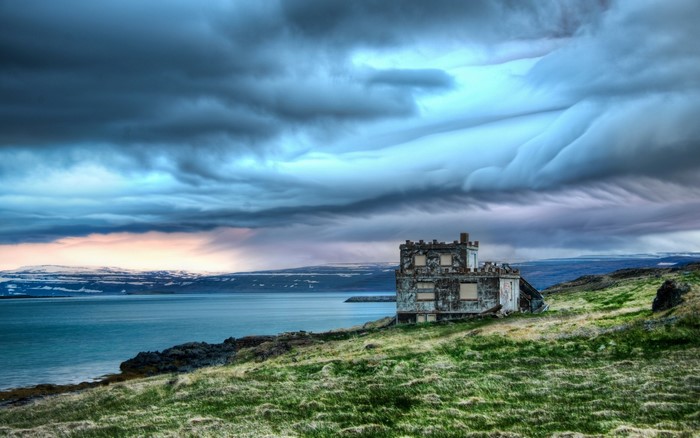 Abandoned building on a grassy coast under stormy clouds