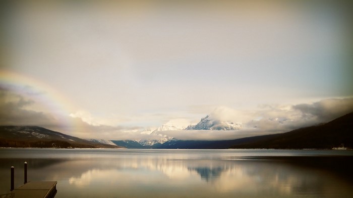Lake and snow-capped mountains with rainbow and dock