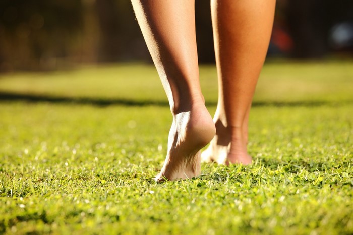 Bare feet walking on green grass in sunlight
