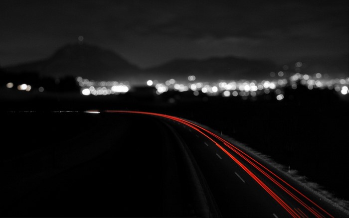 Long exposure of red light trails on a dark road at night with city lights