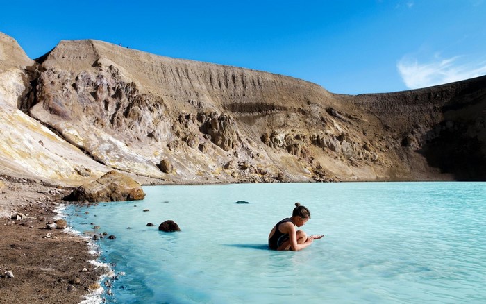 Woman sitting in a turquoise lake with volcanic mountains