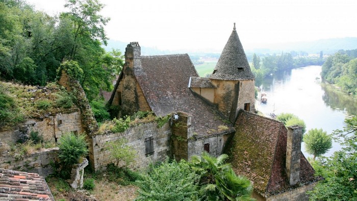 Overgrown stone buildings on a hillside overlooking a river