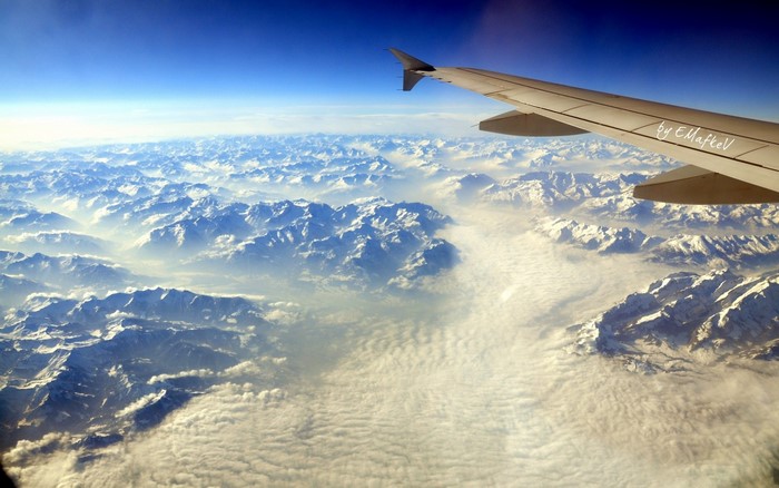Airplane wing over snow-capped mountains and clouds