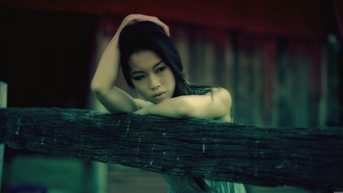 Asian woman with hand in hair leaning on wooden beam