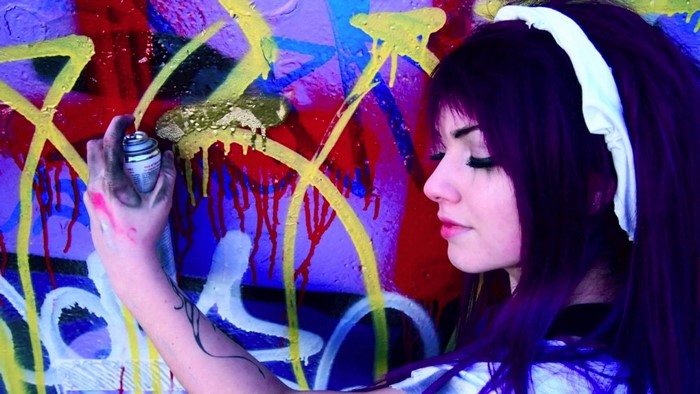 Girl with purple hair spray painting graffiti