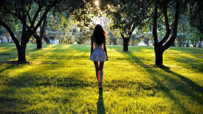 Woman walking in a sunlit park with trees