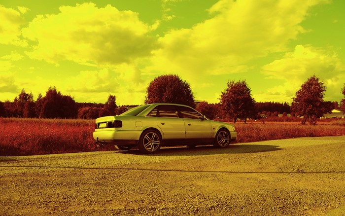 Silver sedan parked on a gravel road with trees and field