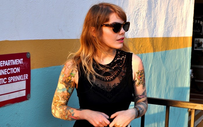 Woman with tattoos and sunglasses in front of a colorful wall