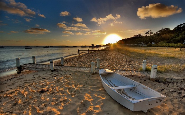 Boat on a sandy beach at sunset with a pier