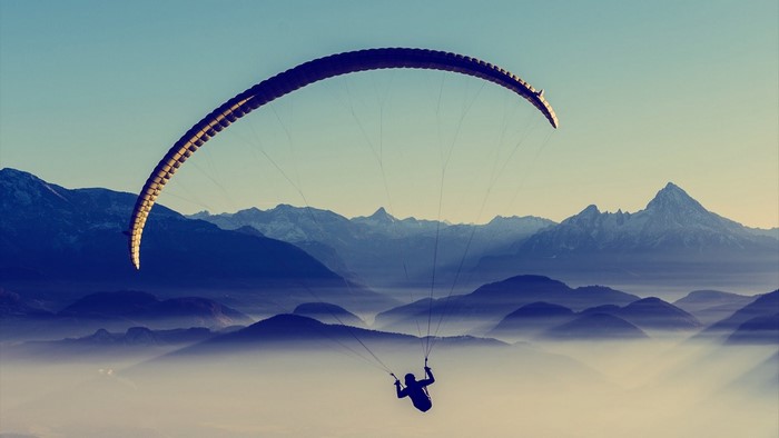 Paraglider flying over misty mountains at sunrise