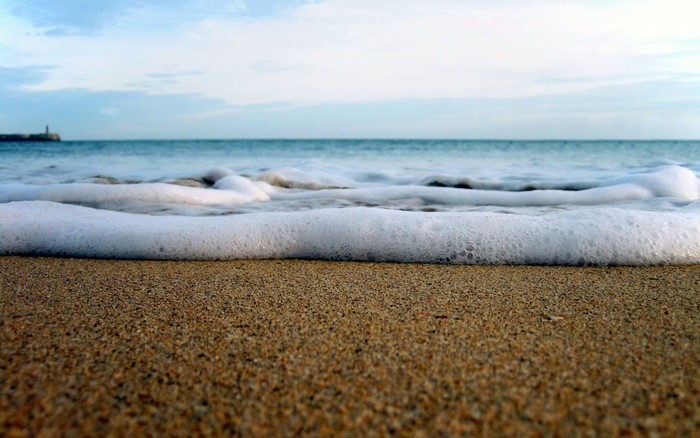 Ocean wave on a sandy beach with a distant lighthouse