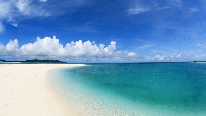 White sand beach and turquoise ocean under blue sky with clouds