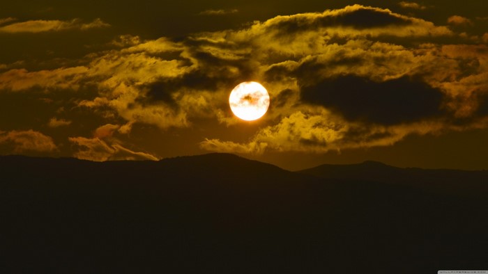 Sun setting behind mountains with dramatic clouds
