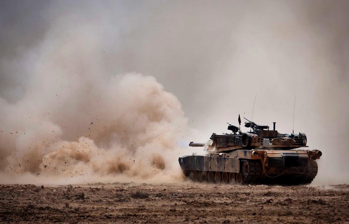 M1 Abrams tank firing in a dusty environment