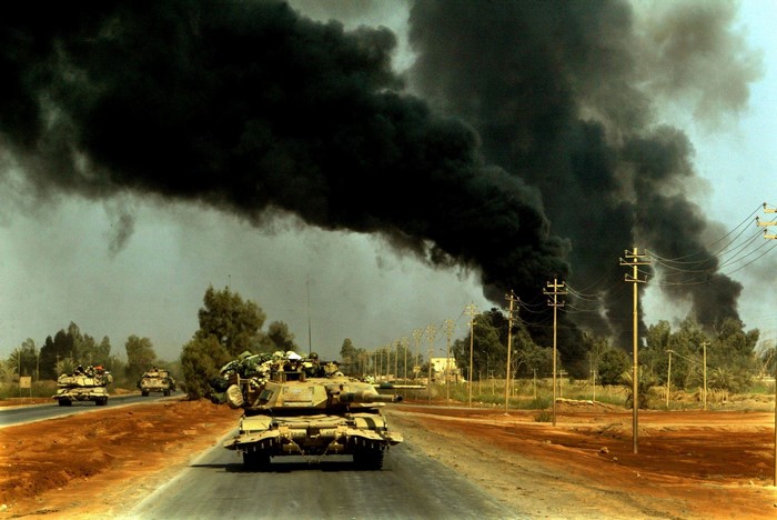 Tanks on a road with black smoke in the background